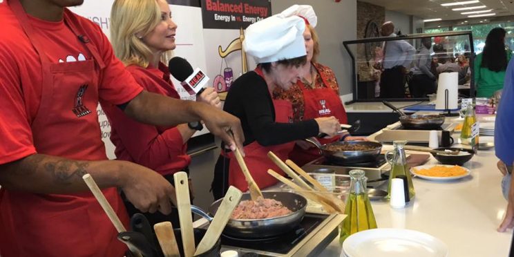 Three Chefs Working Behind Counter While Reporter Talks on Microphone