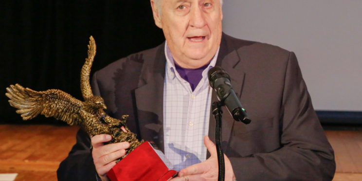Joe Beam, speaks into a microphone while holding his Alumnus of the Year award, a bronzed eagle in flight.