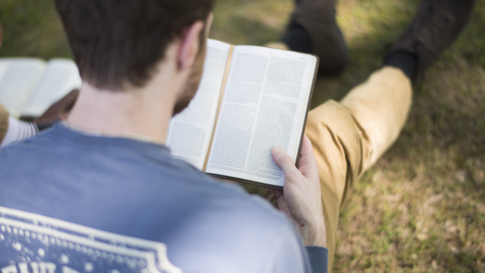 Student reading bible while sitting on grass
