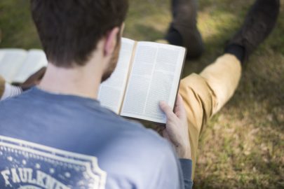 Student reading bible while sitting on grass