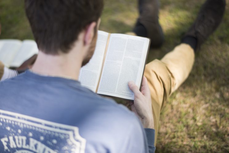 Student reading bible while sitting on grass