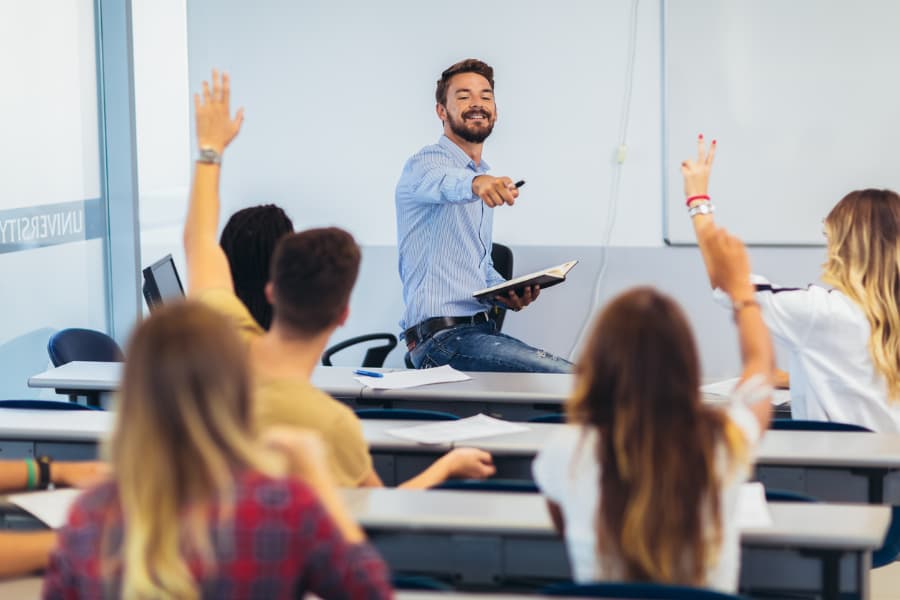 Teacher lecturing in front of classroom with students volunteering