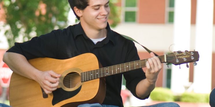 Aaron Reynolds plays his guitar in front of the Harris College of Business.