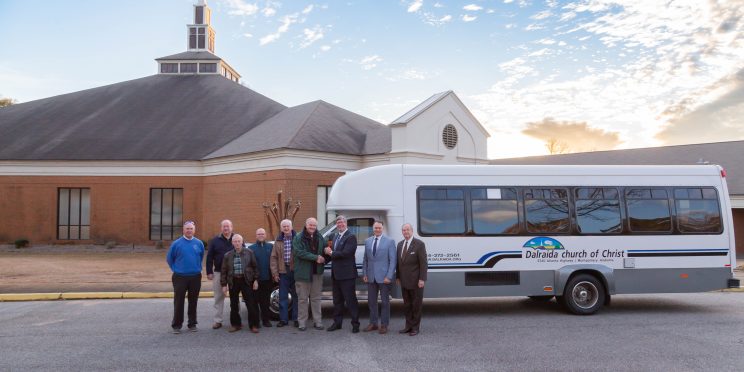 Elders of Dalraida Church of Christ and leaders from Faulkner University post in front of the newly donated bus in front of the church in the parking lot.