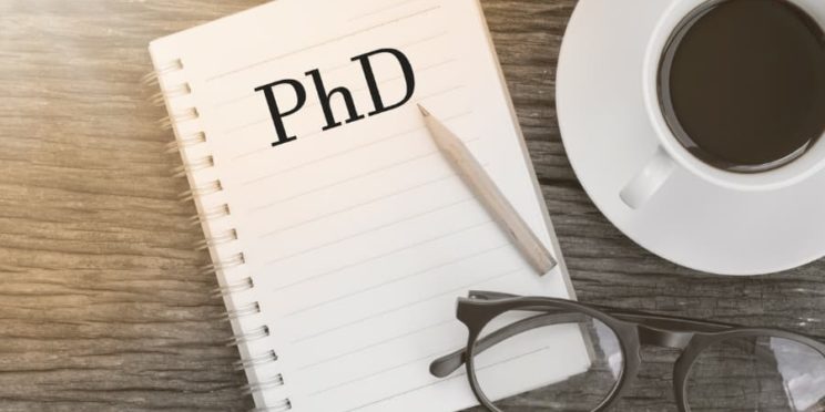 Illustration of coffee cup, glasses, and notebook with “PhD” typed on it