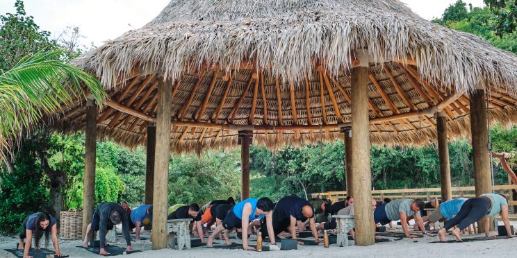 Participants with Heal the Heroes take part in a healing yoga session under a thatched roof hut.