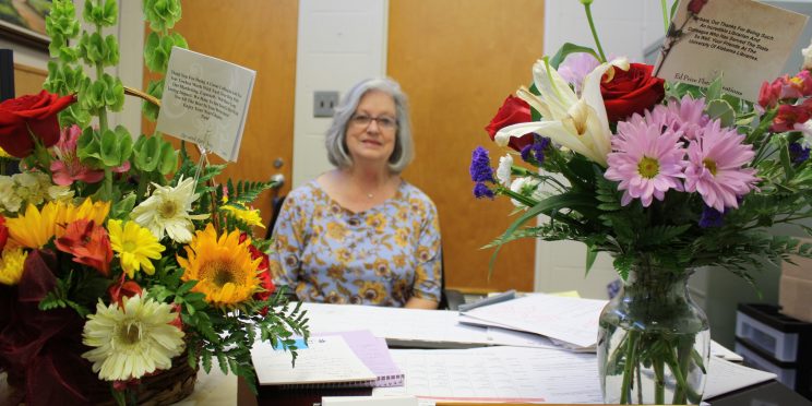 Barbara Kelly sits at her desk surrounded by two large bouquet of flowers.