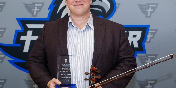 Westley Schlundt holds his violin and award. As a musician, he was honored as the Faulkner Young Alumnus for the Music Department.