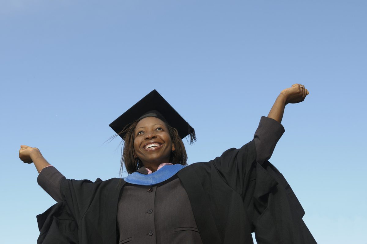 New grad wearing cap and gown triumphantly raises arms