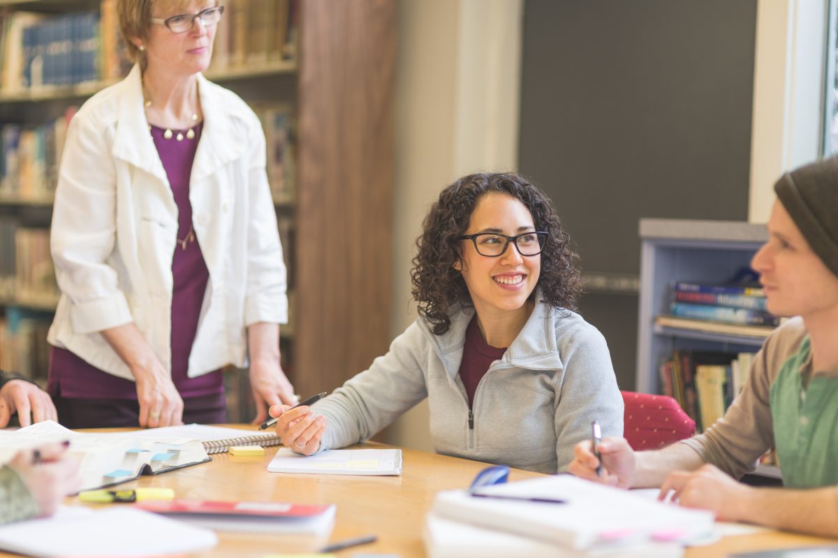 Professor with group of students at table in library