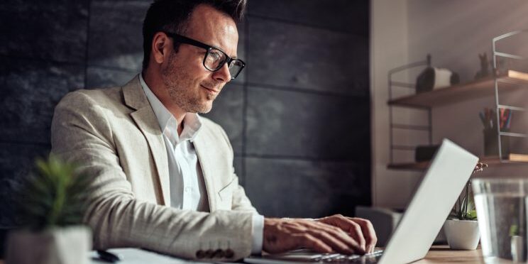 Graduate student in blazer and glasses working on laptop at desk