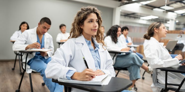 Group of medical students sitting at desks in classroom and taking notes