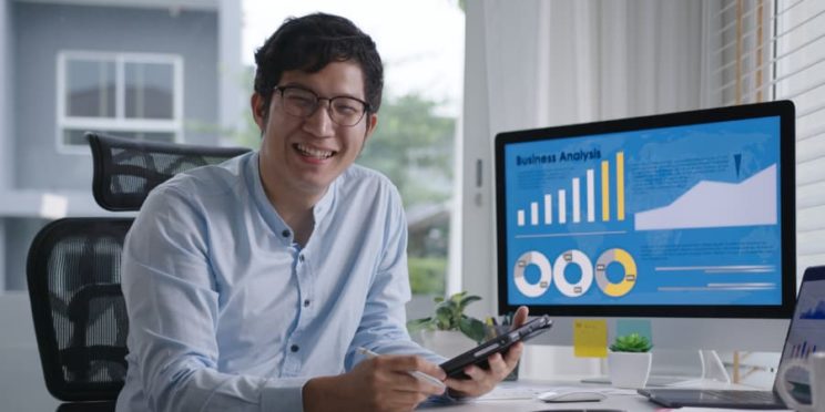 Smiling employee working at computer with analytics on screen