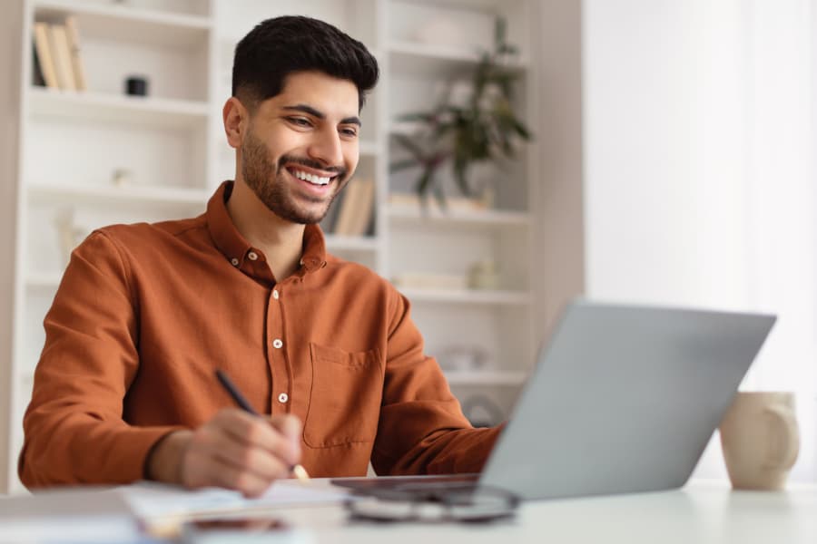 man-studying-online-while-writing-on-notebook