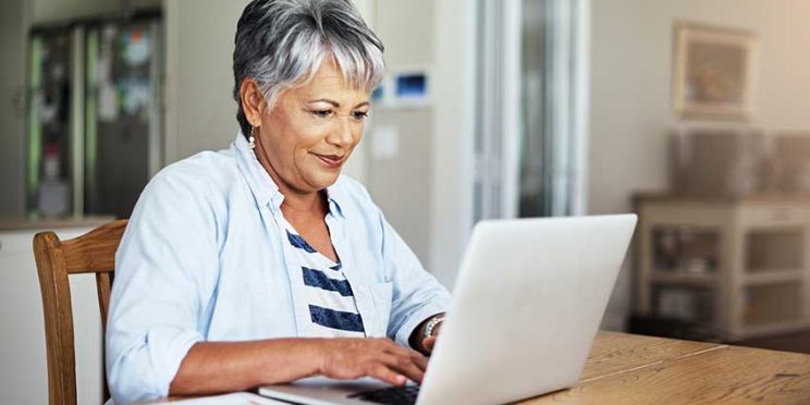 Older Woman Sitting at Table Typing on Laptop