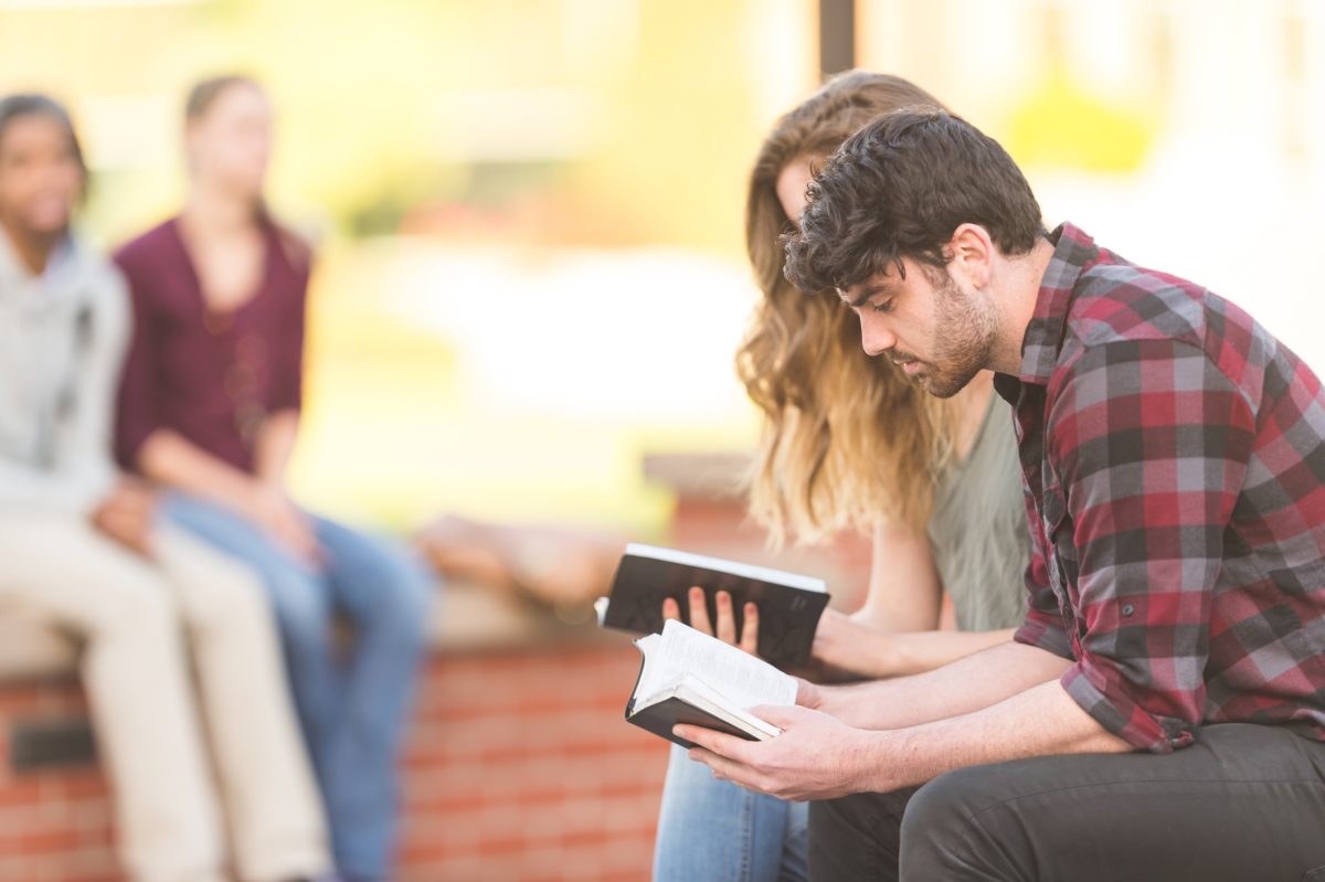 Two college students reading Bible together on park bench outside